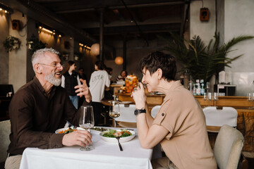 Laughing mature couple dining with glasses of wine and talking in cafe