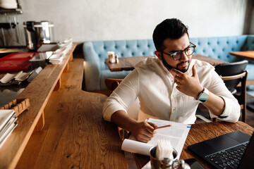 Upset busy indian business owner in eyeglasses working on laptop in cafe