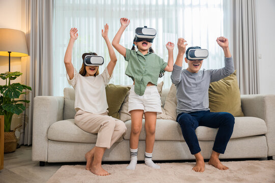 Happy family have mother father and daughter watching movie or playing video game, game entertainment innovation technology, Asian family wear vr glasses headsets excited sitting sofa in living room