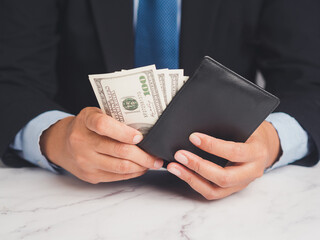 Businessman holding a wallet with US dollar bills while sitting at the table