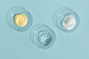 Different textures of cream, serum, gel in Petri dishes on a blue background. The concept of...