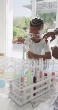 Vertical video of african american father and son holding test tubes with liquid, slow motion