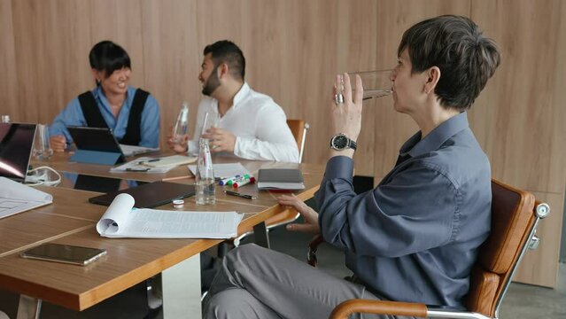 Multinational smiling colleagues drinking water in glasses at office meeting