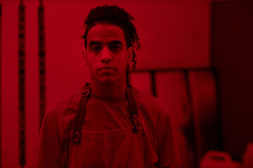 Portrait of young photographer looking at camera while standing in darkroom with red light
