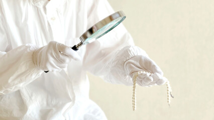 拡大鏡でパールネックレスを見る白手袋の手元_ワイド