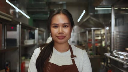 Smiling asian business owner in apron looking at camera in cafe kitchen