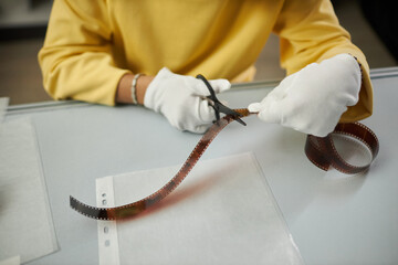 Close-up of photographer in white gloves cutting photo film with scissors while sitting at his...