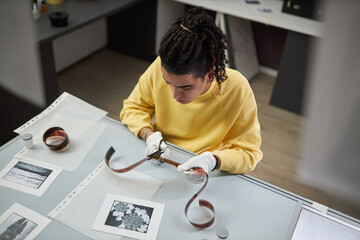 High angle view of young photographer cutting photo film sitting at his workplace in photo studio