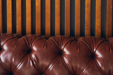 On a wooden background, a close-up of a piece of artificial brown leather, upholstered furniture in...