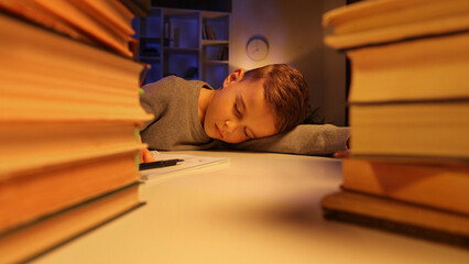 A small schoolboy lies tired from a lot of homework, completes the assignment, falls asleep tired. The concept of children's overload, fatigue from school.