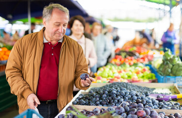 Aged man customer buying plums in open-air market