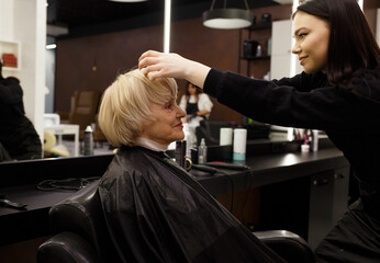 Portrait of an elderly woman visiting a professional hairdresser. An experienced hairdresser does hair styling for a client.