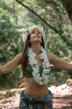 The young hula dancer looking up with open arms receiving the energy of the jungle meditating. Miss Tropical wears a crown and necklace of white flowers.
