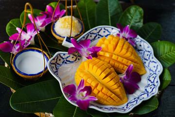 Mango Sticky Rice. Thai dessert (Kwao Neaw Ma-Moung) sweet mango with coconut milk sauce on plate and leaves. Summer tropical asian fruit decorated with orchid.