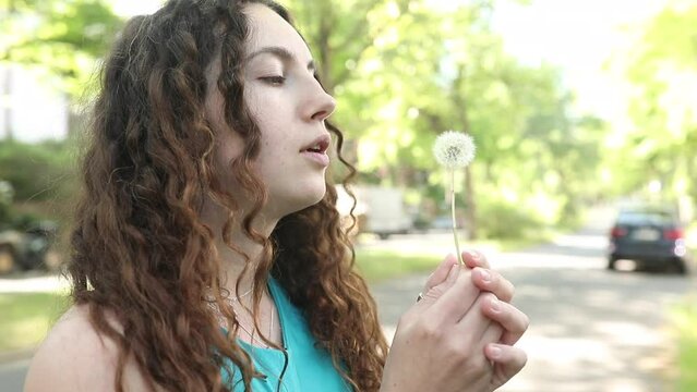 Portrait of a beautiful young woman blowing on the ripened dandelion. 
