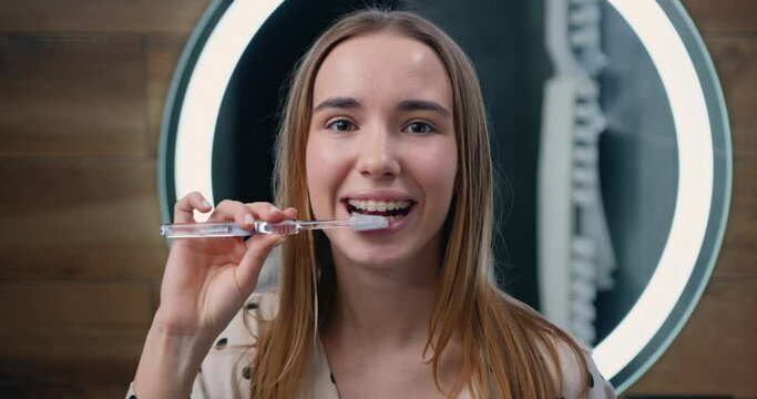 Good-looking 20 years old girl brushing teeth for morning routine and body care.in bathroom at home. Face portrait of happy young woman holding toothbrush brushing teeth looking in camera
