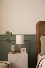 Bedroom interior with marble night table cozy bed, beige bedding, stylish lamp, plants in pots, clock, wall with stucco, carpet and personal accessories. Home decor. Template.