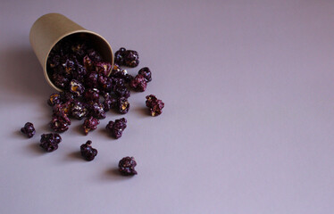 purple popcorn in caramel glaze in a paper cup on a lilac background