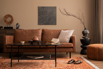 Cozy composition of living room interior with mock up poster frame, brown sofa, black coffee table, stylish pouf, vase with branch, patterned rug and personal accessories. Home decor. Template.