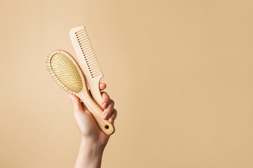 Woman holding two wooden hairbrushes on beige background, hair care, copy space