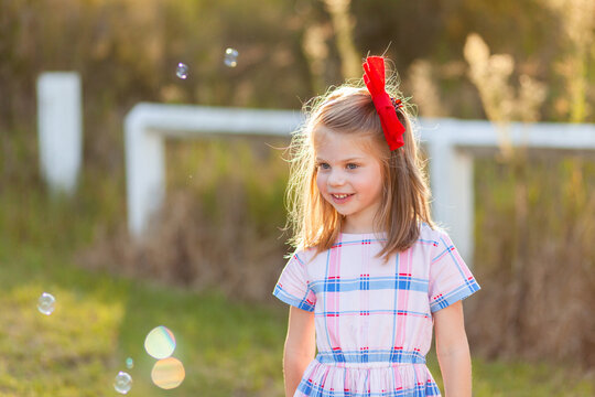 Happy girl with hidden disability standing in sunlight with bubbles at park