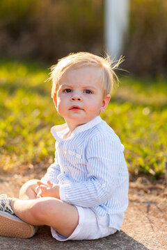 One year old boy sitting on footpath backlit by evening light