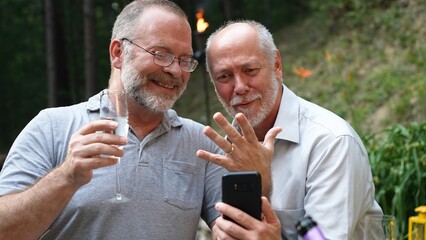 Two gay men have video chat on phone with friends showing their engagement ring for their marriage.
