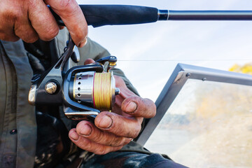 Summer fishing. A fragment of a fishing rod and a spinning reel in the hands of an angler....