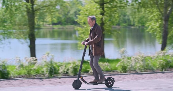 Man rides electric scooter in city park on spring day. Concept of electric transport in city, an environmentally friendly mode of transport.