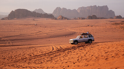Man laying on his jeep in the Wadi Rum desert, large rock formations seen in the background.
