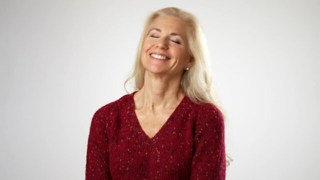 Portrait of middle age mature woman, receives beautiful compliments, finally raises her hands puts hands on chest. Beautiful mature blond isolated on solid white background. Copy space