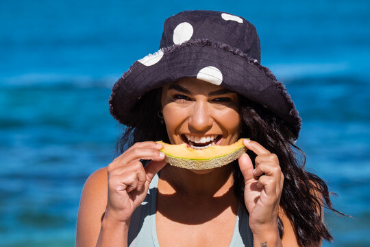 Close up of Young woman wearing full brim hat and eating rockmelon on the beach on clear sunny day
