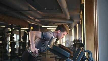 Young athletic man doing dips for chest, shoulders and triceps in fully-equipped gym. Sportsman raises and lowers himself on bars with straight arms. High quality 4k footage