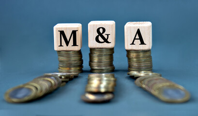 M and A - acronym on wooden cubes against the background of stacks of coins
