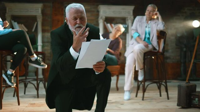 Elderly male actor rehearse the script on stage in front of their colleagues