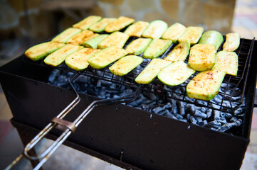 Close-up view of zucchini slices, being seasoned, marinated and cooked over flaming charcoal barbecue grill in a backyard. BBQ party. The concept of preparing food in the open air and summer chill out