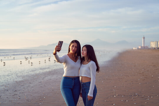 mid adult latina mother and daughter taking a photo with their cell phone on the beach with the La Serena Lighthouse in the background