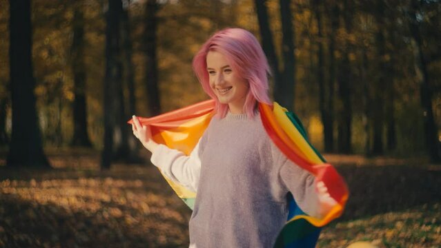 Young happy pink-haired woman holds rainbow flag in park, LGBT pride parade