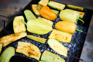 Close-up of fresh marinated seasoned bell peppers and slices of zucchini grilling on grate over charcoals in the barbecue grill. BBQ party. Preparing delicious food outdoor. Weekend leisures. Picnic