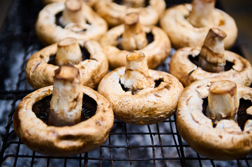 Close-up view of delicious tasty seasoned marinated brown champignon portobello mushrooms, being cooked over flaming charcoal barbecue grill in the backyard BBQ party. Picnic. Cookout. Food still life