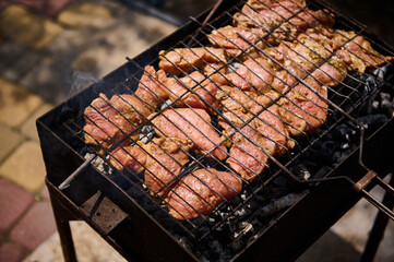 View from above of marinated pork tenderloin grilling on the grate over coals on barbeque grill outdoors. Food background. Food preparations. Selective focus