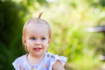 Baby girl against green backdrop outside with hair in topknot crest