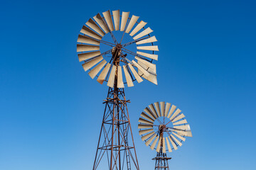 Looking up at wo large windmills against a blue cloudless sky