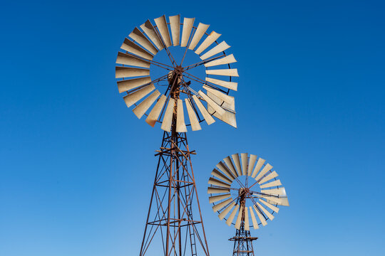 Looking up at wo large windmills against a blue cloudless sky