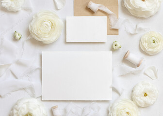 Obraz na płótnie Canvas Blank cards near cream roses and white silk ribbons top view, wedding mockup
