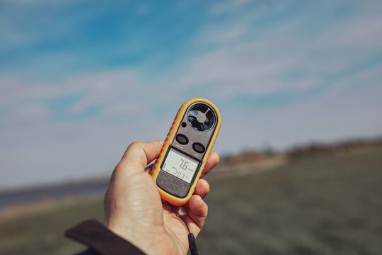 Person holding modern digital anemometer outdoors for measuring wind speed, temperature, humidity and other atmospheric effects.