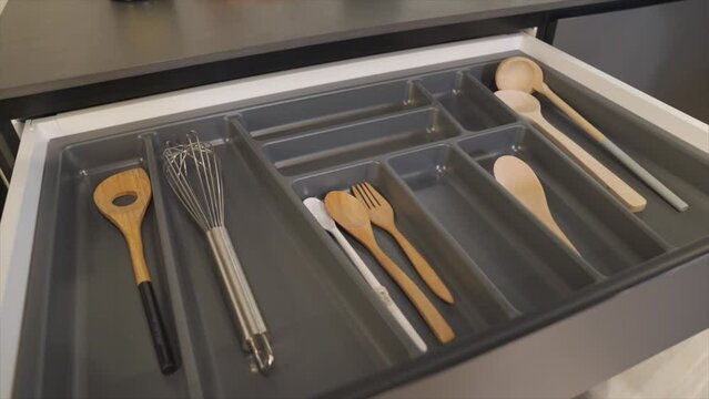 Different utensils in open desk drawer indoors, close up. Kitchen utensil such as spoon, ladle, scoop, handshake stored in box.