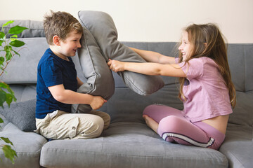 Little boy and girl play pillow fight on the couch. Happy childhood.