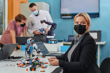 A woman wearing a protective mask standing in a laboratory while her colleagues test a new robotic...