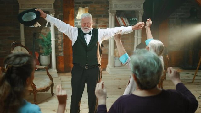 The happy old stand-up comedian enjoys dancing on stage with cheerful support from the audience. 